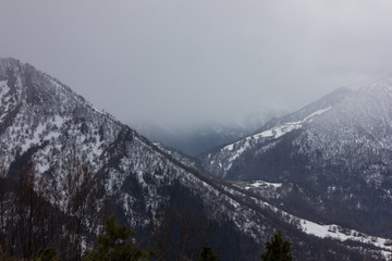Snow-capped mountains in the fog. Caucasian ridge at the beginning of winter. The first snow in the mountains of Russia.