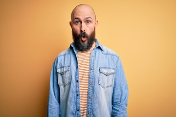 Handsome bald man with beard wearing casual denim jacket and striped t-shirt afraid and shocked with surprise expression, fear and excited face.