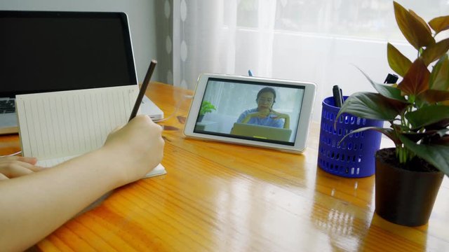 A young Asian woman is sitting down to take notes while meeting online via Smart Device.