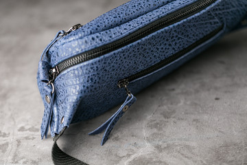 Waist bag made of blue leather, banana on a gray background.