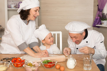 Mom, dad and little son cook together in quarantine. The family laughs and cooks pizza in cookery suits.