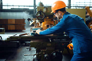 Worker in uniform and helmet works on lathe, plant