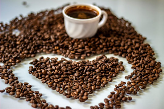 Coffee cup filled with coffee beans and a heart of coffee beans. Coffee beans in the shape of a heart isolated on a white background. Heart shape made of perfect coffee beans, copy space.