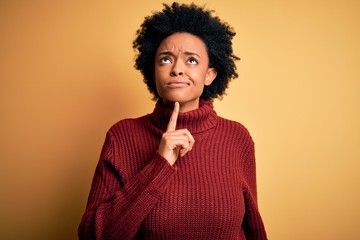Young beautiful African American afro woman with curly hair wearing casual turtleneck sweater Thinking concentrated about doubt with finger on chin and looking up wondering