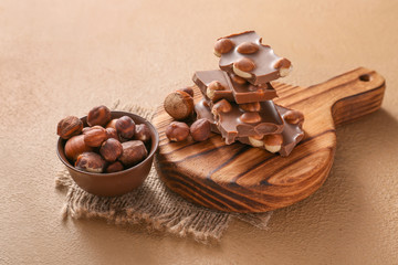 Tasty chocolate with hazelnuts on color background
