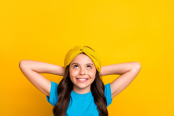 Naklejka premium Closeup photo of beautiful little lady model hold arms behind head resting good mood looking up empty space dreamer wear casual blue t-shirt headband isolated yellow color background