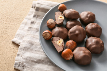 Plate with tasty chocolate candies and hazelnuts on table
