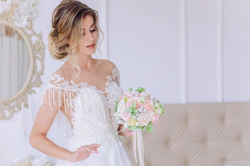 Fototapeta na wymiar Beautiful bride with a wedding bouquet in a beautiful white room, catalog of wedding dresses, beautiful bride waiting for the groom, portrait of the bride, single bride in a beautiful dress