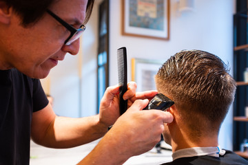 Barber trims the hair of young man with a razor