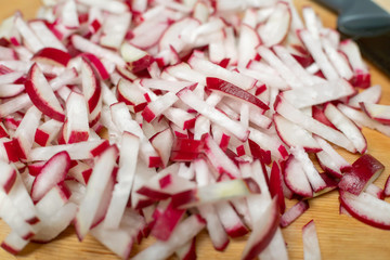 Sliced radishes for salad in close-up on a wooden Board next to a knife.