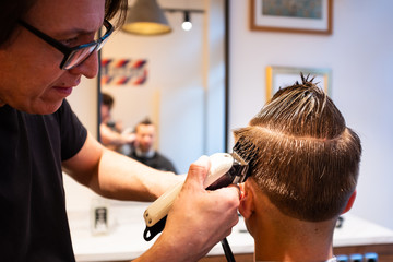 Barber trims the hair of young man with a razor