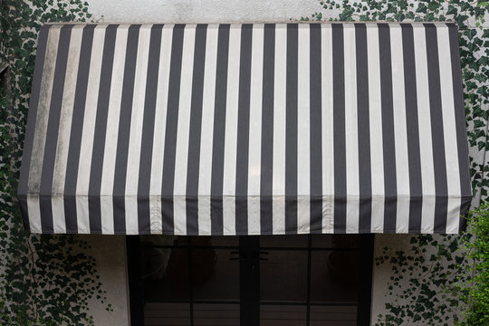 old dirty canvas awning. grungy black and white striped awning over entrance door of shop.