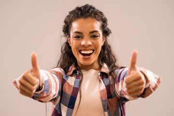 Studio shot portrait of beautiful happy african-american ethnicity woman in casual clothing showing thumb up.