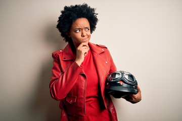 Young African American afro motorcyclist woman with curly hair holding motorcycle helmet Thinking worried about a question, concerned and nervous with hand on chin