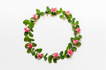 Round circular wreath with green plant branches and pink roses on white background.