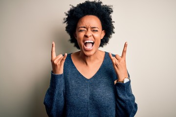 Young beautiful African American afro woman with curly hair wearing casual sweater shouting with crazy expression doing rock symbol with hands up. Music star. Heavy music concept.
