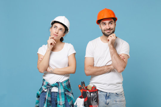 Pensive couple woman man in casual clothes protective helmet hardhat isolated on blue background. Instruments accessories for renovation apartment room. Repair home concept. Put hands prop up on chin.