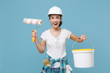 Excited young woman in protective helmet hardhat hold paint bucket, roller for wall painting...