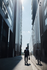 Figure of man walking along tall glass buildings