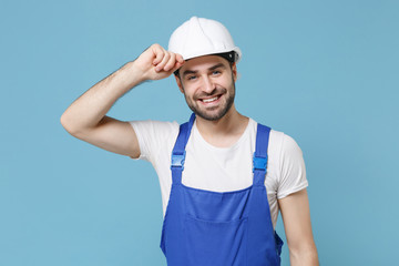 Smiling young man in coveralls protective helmet hardhat isolated on pastel blue background studio portrait. Instruments accessories for renovation apartment room. Repair home concept. Looking aside.