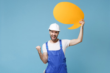 Joyful man in coveralls helmet hardhat hold blank Say cloud speech bubble isolated on blue...