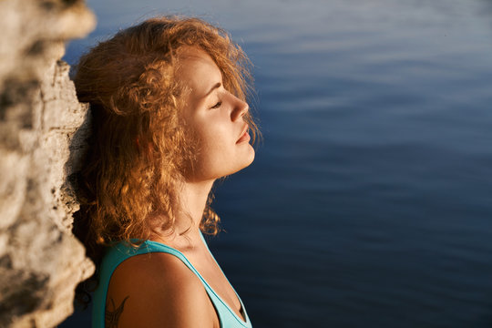 Girl with closed eyes meditating near rock and water.