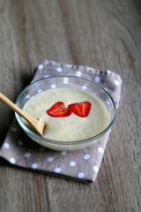 Bowl of vegan banana nice cream with strawberry toppings, polka dot napkin and wooden spoon. Selective focus.
