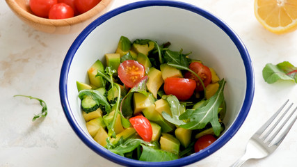 Salad with avocado, tomato, arugula, cucumber and olive oil in bowl