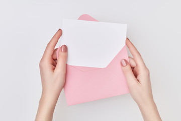 Fototapeta premium Pink envelope with blank white postcard in woman's hands on the white background. Mail concept