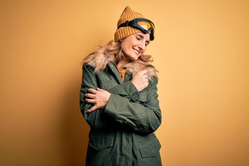 Middle age beautiful blonde skier woman wearing snow sportwear and ski goggles Hugging oneself happy and positive, smiling confident. Self love and self care