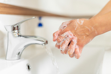 Man or woman washes hands with soap while standing at the sink in the bathroom.