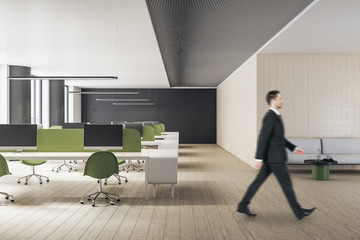 Businessman in suit walking in minimalistic office interior with computers. Workplace and lifestyle concept.
