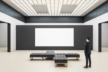 Businessman looking on blank poster in modern gallery interior.