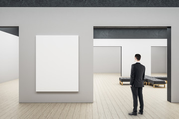 Businessman looking on blank billboard in minimalistic gallery interior.