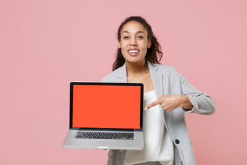 Smiling african american business woman in grey suit white shirt isolated on pink background. Achievement career wealth business concept. Pointing index finger on laptop pc computer with empty screen.