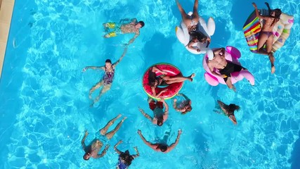 Aerial of friends having party in swimming pool with inflatable flamingo, swan, mattress. Happy young people relax at luxury resort on sunny day. View from above. Girls in bikini sunbathing in a sun. - Powered by Adobe
