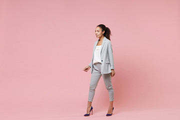 Beautiful smiling young african american business woman in grey suit, white shirt posing isolated on pink background. Achievement career wealth business concept. Mock up copy space. Looking aside.