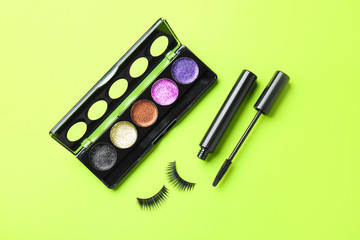 Mascara with fake eyelashes and eyeshadows on color background
