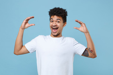 Excited young african american guy in casual white t-shirt posing isolated on blue background studio portrait. People lifestyle concept. Mock up copy space. Showing blah blah gesture ja jaja hands. © ViDi Studio