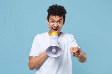 Nervous young african american guy in casual white t-shirt posing isolated on blue wall background. People lifestyle concept. Mock up copy space. Scream in megaphone, pointing index finger on camera.