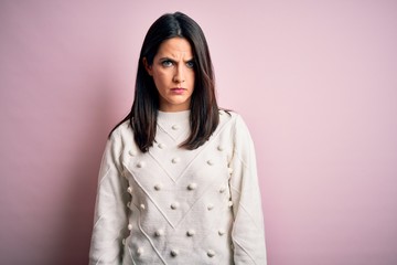 Young brunette woman with blue eyes wearing casual sweater over isolated pink background skeptic...
