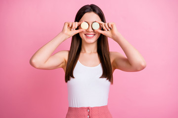 Photo of charming funny lady hold two macaroons cookies hiding eyes like specs playful mood wear white singlet dotted skirt isolated pastel pink color background