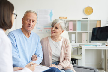 Fototapeta premium Portrait of modern senior couple listening to female doctor while visiting clinic, copy space