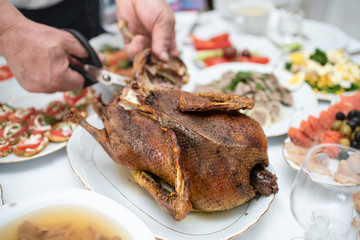 Man divides with scissors freshly baked duck into portions, process close up. Events take place at home during a family meeting to celebrate the solemn event. Foods and dishes on the table