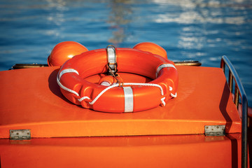 Close-up of an orange boat with life belt, electric lamp for localization and two work helmets, blue water on the background