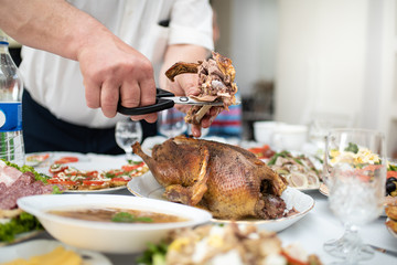Man divides with scissors freshly baked duck into portions, process close up. Events take place at home during a family meeting to celebrate the solemn event. Foods and dishes on the table
