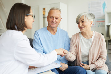 Portrait of modern senior couple shaking hands with female doctor and smiling while visiting private clinic
