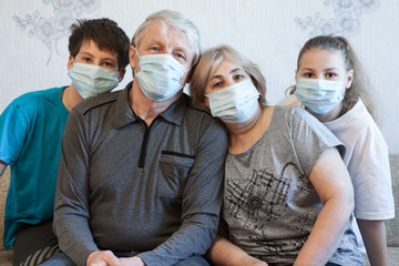 Fototapeta na wymiar Four people portrait, grandparents with their teen age grandchildren wearing facial masks, sitting on sofa in a domestic room