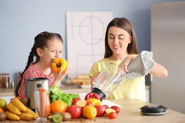 Mother and little daughter with ingredients for smoothie and blender in kitchen