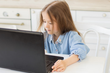 Pretty preschool girl studing at home with digital table laptop.